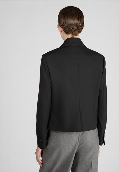 Blazer nero sartoriale, caratterizzato da un colletto strutturato, maniche lunghe e un taglio corto. Tessuto morbido con dettaglio di spacco sul retro.