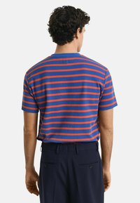 Gestreepte t-shirt in blauw en rood, korte mouwen, ronde hals, relaxte pasvorm. Draag met marineblauwe broek, vanuit een achteraanzicht. Textured katoen materiaal.