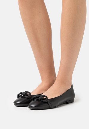 Schwarze Leder-Ballettschuhe mit abgerundeter Zehenpartie, die an der Vorderseite mit einer dekorativen schwarzen Kettenverzierung und einem flachen Absatz ausgestattet sind.