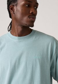 Lys blå bomulds t-shirt med korte æermer og rund halsudskæring. Har subtilt broderet "Levi's" logo på brystet. Glat tekstur.