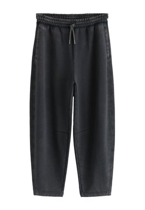 Close-up van een persoon die zwarte joggingbroek met elastische taille, trekkoord en zijzakken draagt, hand gedeeltelijk in de zak.