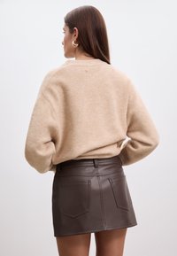 Pull en mélange de laine beige à coupe décontractée, associé à une mini-jupe en similicuir marron avec deux poches à l'arrière et une taille ajustée.