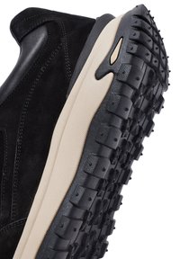 Sneaker in suede e pelle nera con una suola intermedia color crema, caratterizzata da una suola in gomma nera testurizzata con motivi del battistrada prominenti.