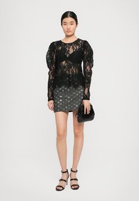 Haut en dentelle noire à manches longues et bouffantes, associé à une mini-jupe à paillettes. Accessoirisé avec un petit sac noir et des talons noirs à lanières.
