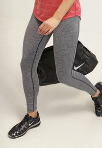 Szare legginsy sportowe o teksturowanym wykończeniu i czarnym bocznym pasku, w połączeniu z czarnymi sneakersami i czarną torbą na siłownię z logo.