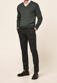 Sweter z dekoltem w serek w ciemnozielonym dzianym materiale, zestawiony z czarnymi, dopasowanymi spodniami oraz czarnymi skórzanymi botkami Chelsea. Tkanina wydaje się gładka i trwała.