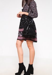 Vestido floral negro con mangas largas, dobladillo estampado, combinado con un bolso negro tipo cubo y botas negras hasta el tobillo. Tela suave con acentos florales.