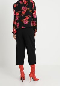 Blusa nera a fiori con colorate rose e arancioni, abbinata a pantaloni neri a gamba larga e stivaletti rossi al ginocchio con tacco a spillo.