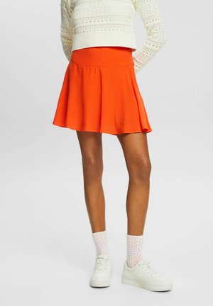Jupe patineuse orange avec une texture lisse et un design évasé, associée à des chaussettes blanches à motifs et des baskets blanches.