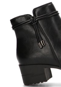 Bota de cuero negro hasta el tobillo con punta redondeada y tacón bajo. Presenta un nudo decorativo y acentos metálicos cerca de la cremallera.