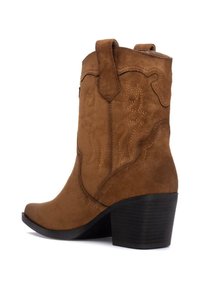 Botas de vaquero de ante marrón con costuras decorativas, punta afilada y un tacón negro apilado. Cuenta con lazos de tirón para poner y quitar fácilmente.