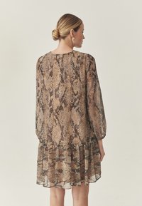 Fließendes Kleid mit Schlangenledermuster, das lange Ärmel, einen Rundhalsausschnitt und einen gerüschten Saum aufweist. Die Farben umfassen verschiedene Brauntöne und Beige.