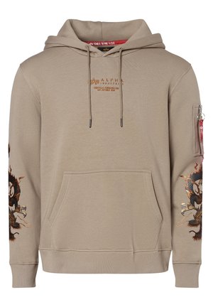 Beżowa bluza z kapturem Alpha Industries z kieszenią z przodu, motywami smoków na rękawach, kapturem z troczkami oraz kieszenią na zamek błyskawiczny z czerwonym tagiem na lewym ramieniu.