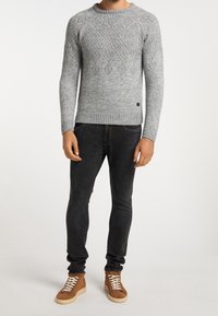 Maglione grigio lavorato a maglia con motivo a rombi, polsini e bordo a coste, abbinato a jeans neri slim-fit e sneakers alte marroni.