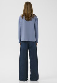 Felpa oversize di colore azzurro chiaro con spalle scese abbinata a jeans in denim blu scuro a gamba larga. Tessuto morbido e vestibilità rilassata.