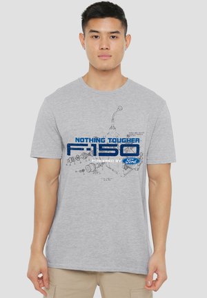 Man wearing light gray t-shirt with blue text "Nothing tougher F-150 powered by Ford" and mechanical blueprint graphic.