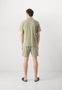 Light green textured short-sleeve shirt and matching shorts with horizontal stripes. Casual design, paired with dark sandals.