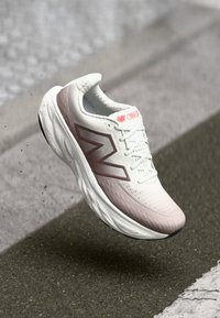 Baskets de sport blanches et roses avec une tige texturée, conception légère, logo 'N' maroon prominent et semelle rembourrée pour un soutien.