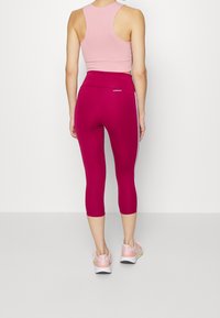 Rosenrød crop top parret med magenta leggings med hvide sidelister, tætsiddende design og blød tekstur. Båret med lyserøde sportssko.