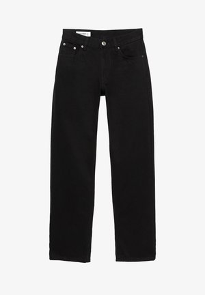 Femme portant une veste bomber noire, une chemise grise boutonnée, un pantalon droit noir et des mocassins en cuir noir, debout sur un fond blanc.