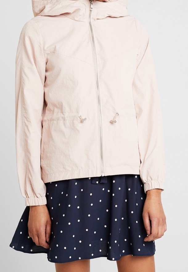 Ljusrosa jacka med huva, dragkedja fram och elastiska ärmslut. Har dragsko vid midjan. Bärs över en marinblå kjol med prickar.