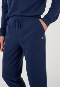 Pantaloni jogger blu navy realizzati in tessuto testurizzato, dotati di vita elastica con cordoncino e tasche laterali; piccolo logo decorativo.