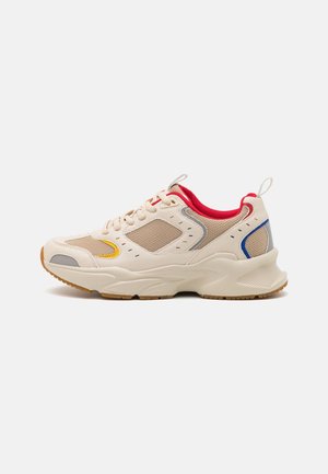 Baskets beige et sable avec doublure intérieure rouge, lacets à l'avant, détails d'accent jaune et bleu, et semelle épaisse blanche sur fond blanc.