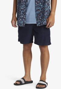 Navy corduroy shorts with a relaxed fit, paired with a floral short-sleeve shirt and black sandals featuring a white striped accent.