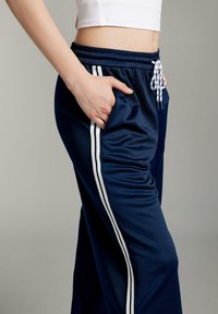 Marina atletiska joggers i slät tyg med vita sidolinjer, elastisk midja och en framficka med dragsko.