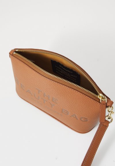 Bolso de cuero marrón claro con un acabado texturizado, cierre de cremallera y una correa desmontable. "THE BEAUTY BAG" grabado en un tono más claro en la parte delantera.