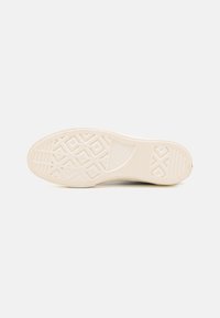 Suola di sneaker beige chiaro con una superficie in gomma texturizzata, caratterizzata da un motivo a diamante e dettagli di branding vicino al tallone.