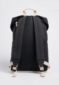 Mochila de tela negra con un respaldo de malla, correas beige, parte superior redondeada y un asa de transporte prominente. Cuenta con herrajes de correas ajustables.