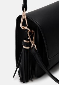 Černá kožená kabelka přes rameno se zlatým zapínáním, s opleteným střapcem a hladkou strukturou těla.