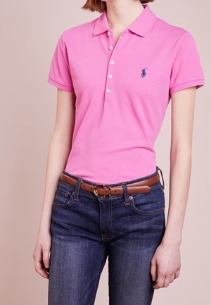 Roze poloshirt met een kraag, drie knopen en een klein geborduurd logo. Draagt met donkerblauwe spijkerbroek en een bruine riem.