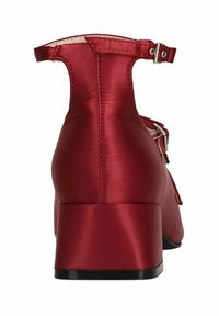 Chaussure à talon bloc en satin rouge avec bride au cheville et boucle. Texture lisse, bout rond, et semelle noire contrastante, mettant en avant des détails de design simples.
