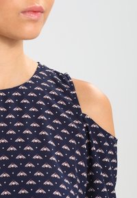 Navy blouse with floral pattern, cold shoulder design, and polka dots. Lightweight fabric with a smooth texture and subtle sheen.