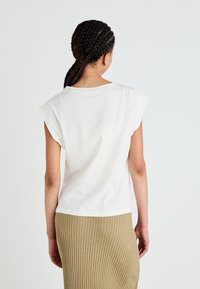 T-shirt bianca in cotone con maniche a sbuffo, scollatura rotonda e vestibilità rilassata, abbinata a una gonna beige a coste lunghezza ginocchio.
