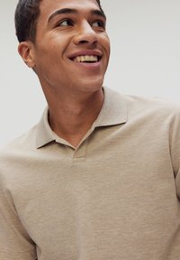 Beige polo skjorta med krage, strukturerad tyg och korta ärmar. Ser delvis knäppt ut med en ren, minimalistisk design.
