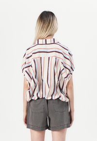 Kragenhemd mit kurzen Ärmeln und vertikalen Streifen in Olivgrün, Rost und Himmelblau, aus leichtem Stoff; kombiniert mit grauen Shorts.