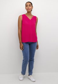 Blusa sin mangas de color rosa con un diseño de escote en V, combinada con jeans de color azul claro y zapatillas blancas, que presenta un corte relajado y una textura suave.