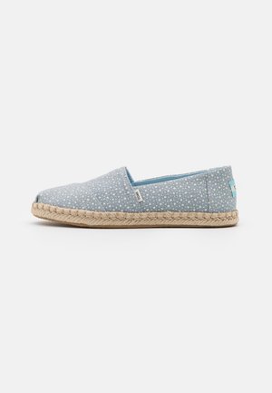 Zapato de tela azul tipo slip-on con lunares blancos, suela de yute natural tejido y un diseño cómodo y minimalista.