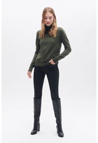 Maglione di lana verde scuro, jeans skinny neri e stivali con tacco alti neri. Design semplice, texture morbida, vestibilità casual. Finitura del tessuto liscia.