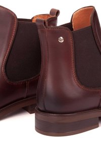 Rjave usnjene gležnarske čevlje z elastičnimi stranskimi paneli, gladko teksturo in nizko nabito peto. Imajo srebrni logotip na strani.