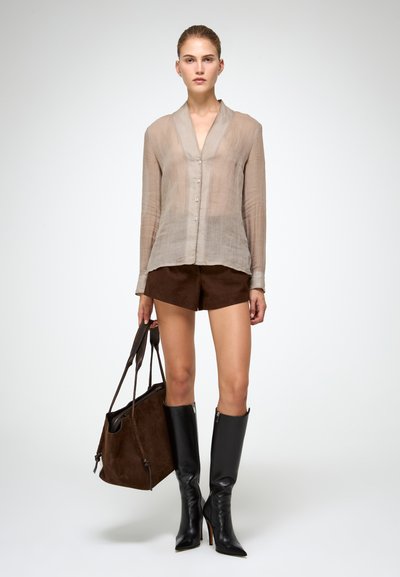 Camicia trasparente beige con bottoni, pantaloni corti in suede marrone, stivali alti fino al ginocchio neri con tacco a spillo e una grande borsa a spalla in suede marrone.