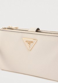 Beżowy skórzany woreczek o fakturowanej powierzchni, z trójkątnym logo w złotym odcieniu i zamknięciem na zamek błyskawiczny, charakteryzujący się gładkim wykończeniem i subtelnym, tłoczonym wzorem.