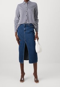 Camicia a righe con maniche lunghe, abbinata a una gonna di jeans lunga fino al ginocchio con uno spacco frontale, accessoriata con una borsa bianca.