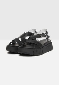 Black platform sandals featuring crisscross leather straps, a rounded toe, and a thick, textured sole with slight grooves. Silver hardware accent.