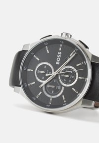 Orologio con cinturino in pelle nera e cassa in acciaio inossidabile. Il quadrante scuro presenta tre sotto-quadranti, indici delle ore argentati e il marchio "BOSS."