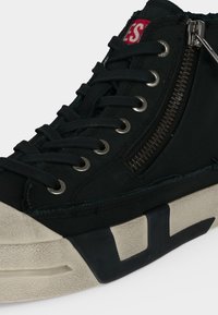 Basket montante noire avec lacets noirs, œillets argentés, semelle beige avec accents noirs et fermeture éclair latérale fonctionnelle.