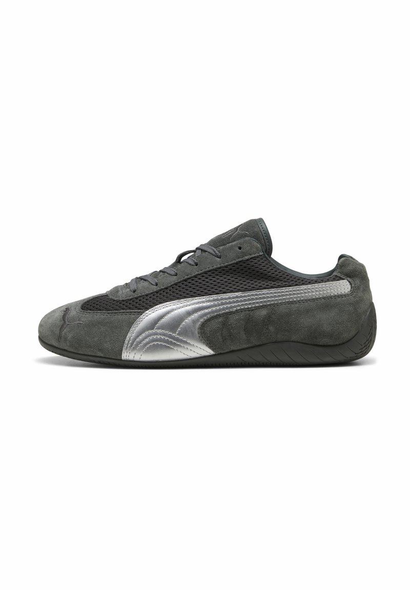 Zapatilla de ante gris con paneles de malla, con una franja de acento plateada y suela de goma negra, diseñada para la comodidad y la flexibilidad.